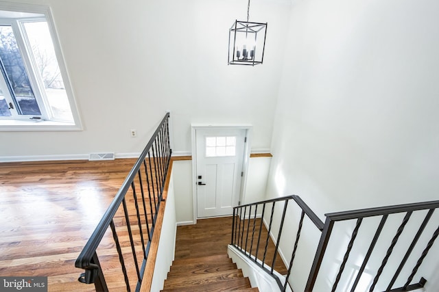 staircase with hardwood / wood-style floors and an inviting chandelier