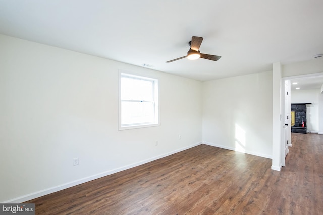 empty room with ceiling fan, a stone fireplace, and dark wood-type flooring