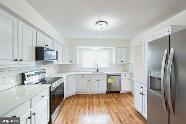 kitchen featuring appliances with stainless steel finishes, light hardwood / wood-style flooring, white cabinetry, and tasteful backsplash