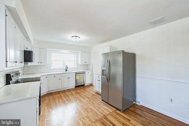 kitchen featuring appliances with stainless steel finishes, tasteful backsplash, sink, light hardwood / wood-style flooring, and white cabinetry