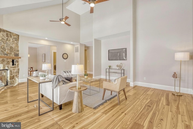 living room featuring high vaulted ceiling, ceiling fan, light hardwood / wood-style flooring, and a stone fireplace