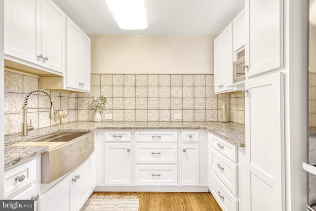 kitchen featuring sink, white cabinetry, light stone countertops, and decorative backsplash