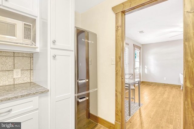 interior space with stainless steel refrigerator, light wood-type flooring, light stone countertops, white cabinets, and backsplash