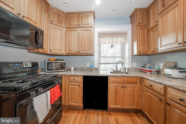 kitchen featuring black appliances, light hardwood / wood-style floors, light stone countertops, and sink