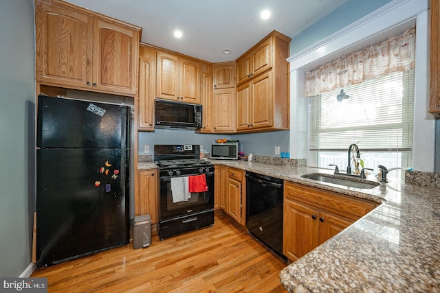 kitchen with light stone counters, light hardwood / wood-style flooring, black appliances, and sink