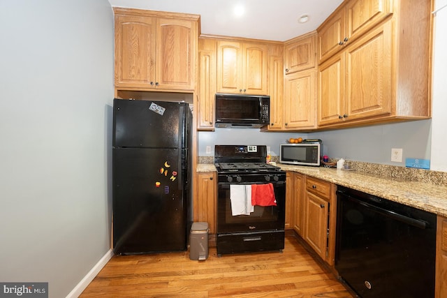 kitchen with light stone countertops, black appliances, and light wood-type flooring