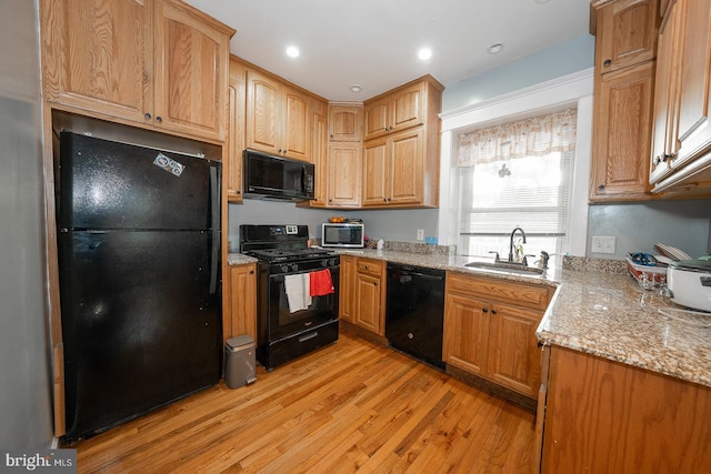 kitchen with light stone countertops, sink, black appliances, and light hardwood / wood-style floors