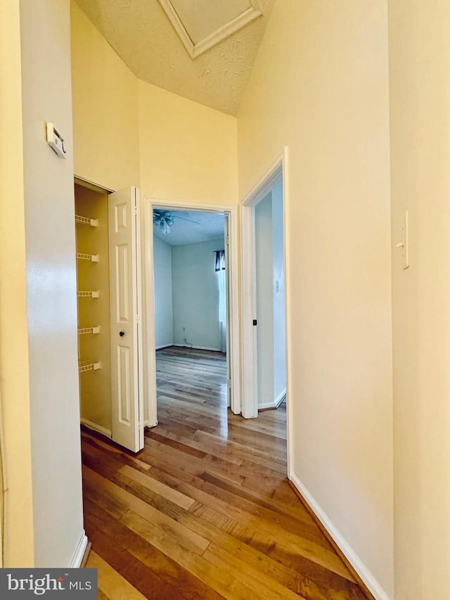 corridor with lofted ceiling, hardwood / wood-style floors, and a textured ceiling