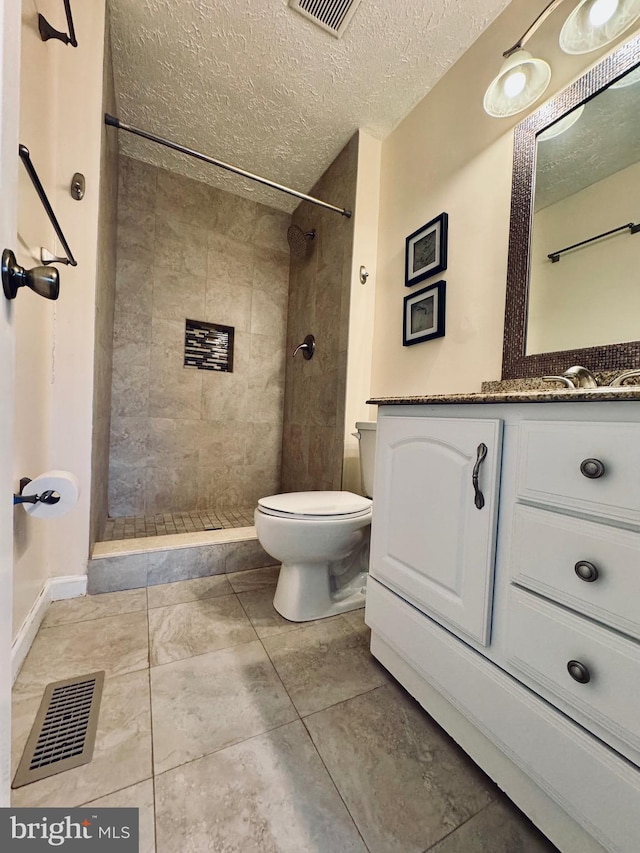 bathroom with vanity, tile patterned flooring, toilet, tiled shower, and a textured ceiling