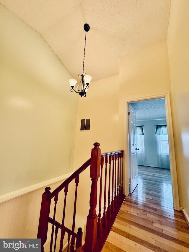 stairs featuring hardwood / wood-style flooring, lofted ceiling, a textured ceiling, and a chandelier