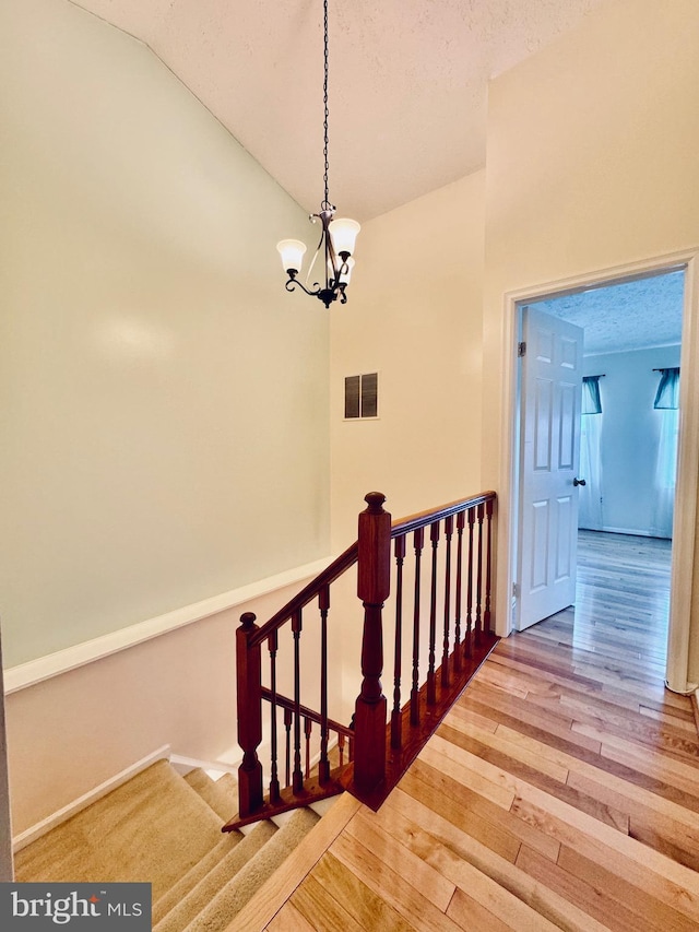 staircase with hardwood / wood-style flooring, a notable chandelier, a textured ceiling, and vaulted ceiling