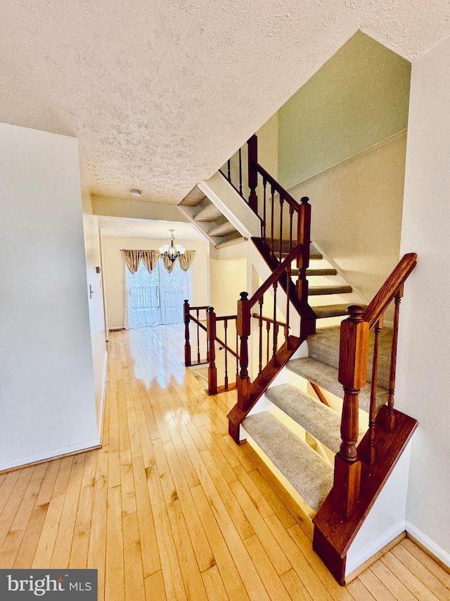 stairs with wood-type flooring, a textured ceiling, and an inviting chandelier