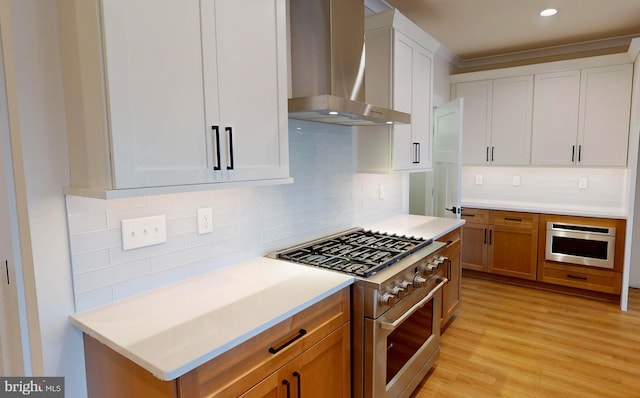 kitchen with white cabinets, stainless steel appliances, wall chimney exhaust hood, and light hardwood / wood-style floors