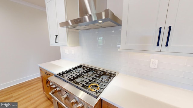 kitchen featuring white cabinetry, decorative backsplash, light hardwood / wood-style floors, and wall chimney range hood