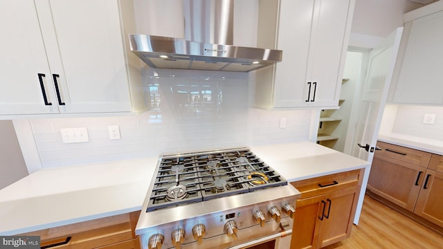 kitchen with white cabinetry, stainless steel range, wall chimney range hood, tasteful backsplash, and light hardwood / wood-style floors