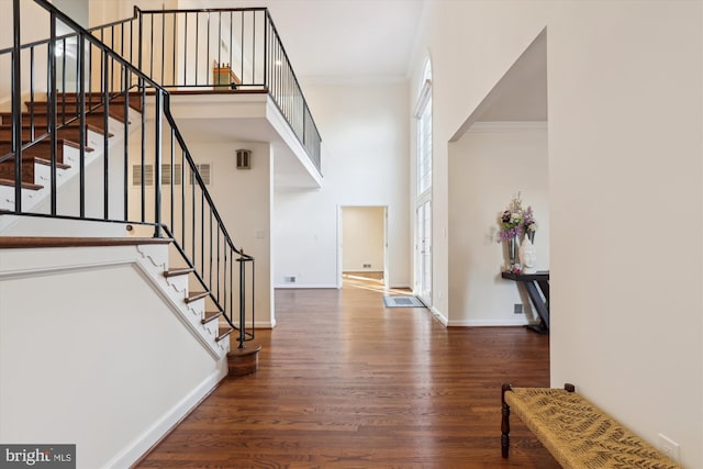 foyer entrance with wood finished floors, stairway, crown molding, baseboards, and a towering ceiling