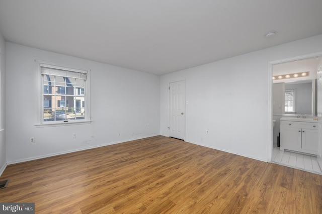 unfurnished bedroom featuring connected bathroom, sink, and light wood-type flooring