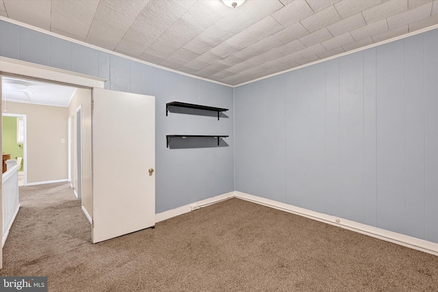 unfurnished room with carpet, crown molding, and wood walls