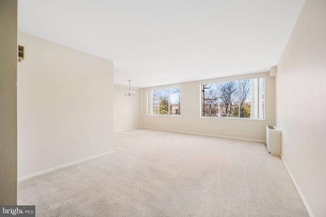 spare room featuring radiator, an inviting chandelier, and light colored carpet