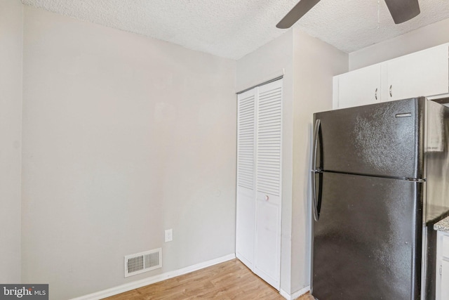 kitchen with white cabinetry, black refrigerator, a textured ceiling, and light hardwood / wood-style flooring