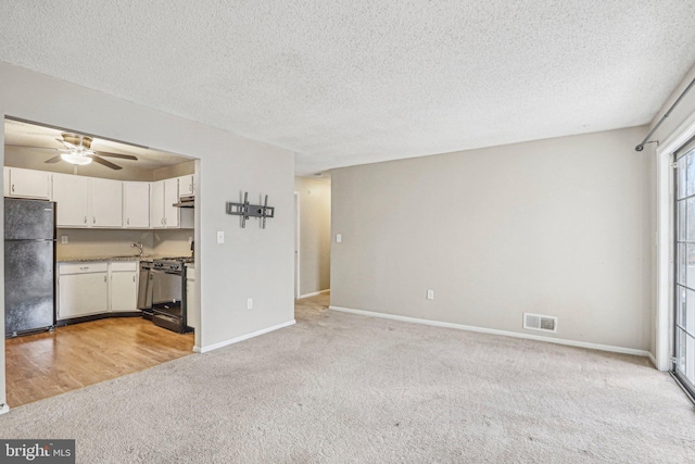 unfurnished living room featuring a textured ceiling, ceiling fan, sink, and light carpet