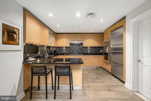 kitchen with a kitchen breakfast bar, sink, built in appliances, light hardwood / wood-style floors, and kitchen peninsula