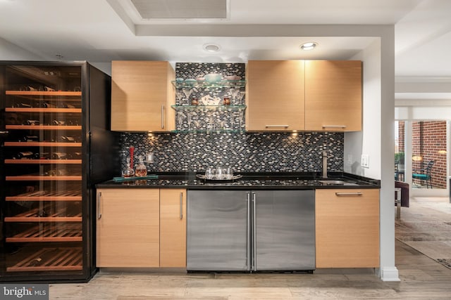 bar with dark stone counters, light brown cabinetry, beverage cooler, and fridge