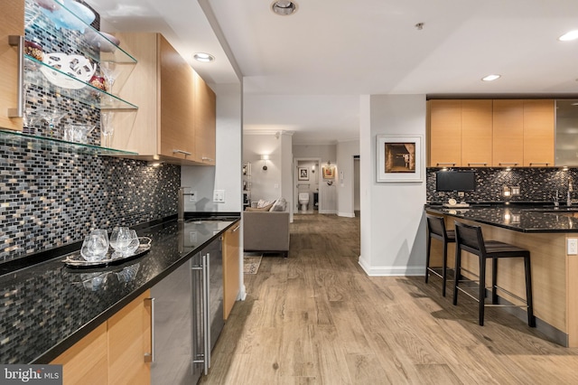 kitchen featuring sink, dark stone countertops, light wood-type flooring, ornamental molding, and tasteful backsplash