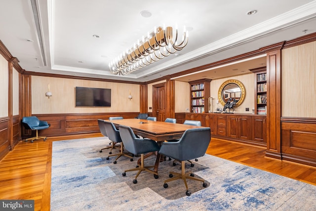 dining area with a raised ceiling, crown molding, an inviting chandelier, built in features, and hardwood / wood-style floors