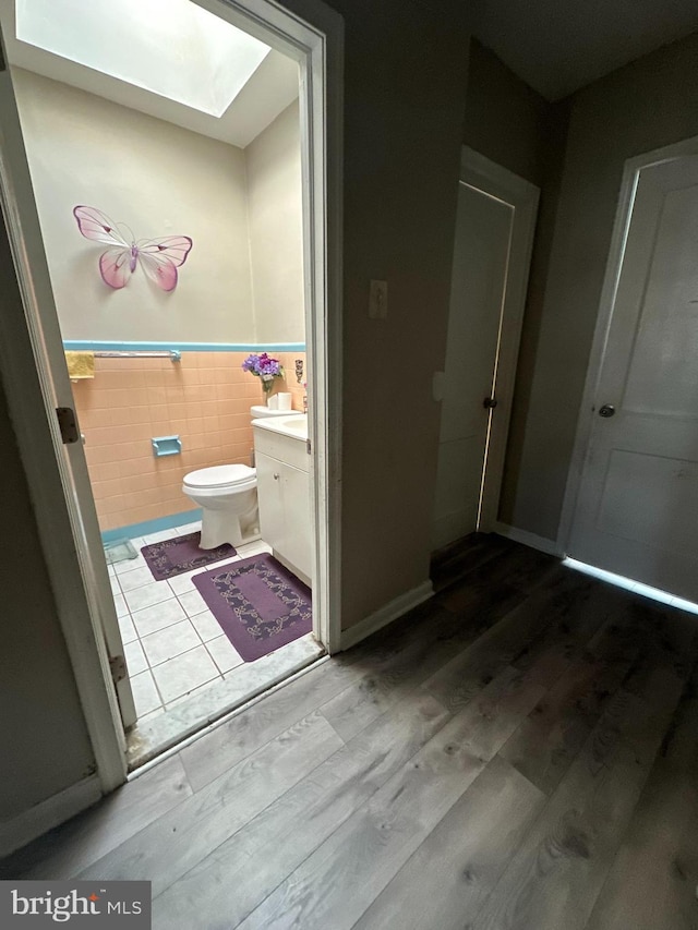 bathroom with vanity, a skylight, hardwood / wood-style flooring, toilet, and tile walls