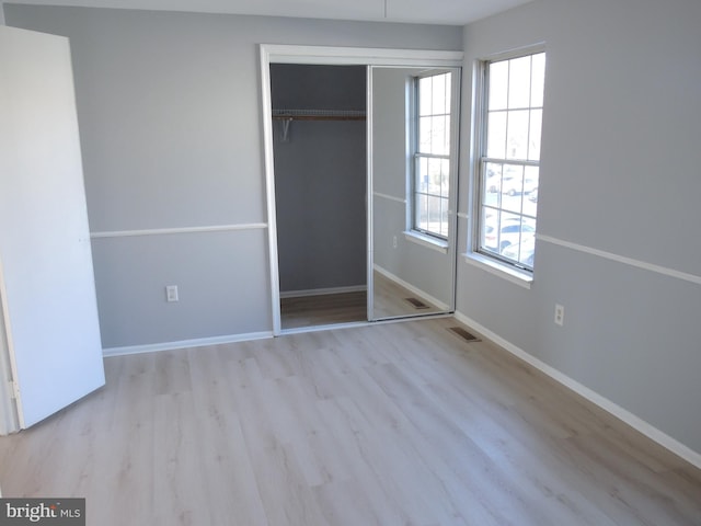 unfurnished bedroom with light hardwood / wood-style flooring, multiple windows, and a closet