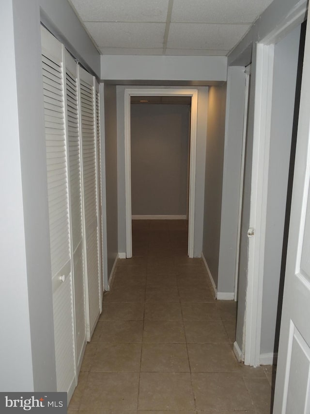 hallway with a drop ceiling and light tile patterned floors