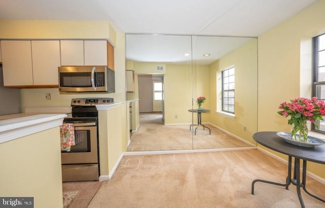 kitchen featuring decorative light fixtures, stainless steel appliances, plenty of natural light, and light colored carpet