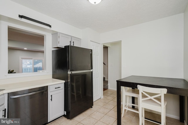 kitchen with black refrigerator, white cabinetry, stainless steel dishwasher, light tile patterned floors, and a textured ceiling