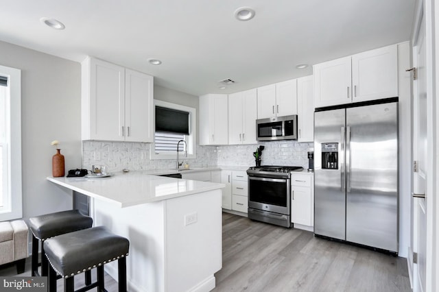 kitchen with kitchen peninsula, light wood-type flooring, stainless steel appliances, white cabinetry, and a breakfast bar area