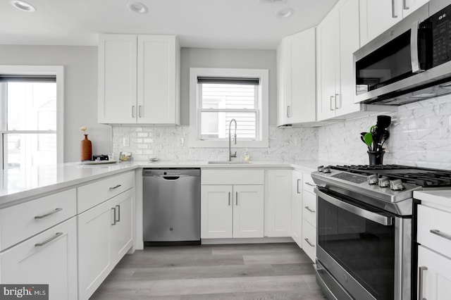 kitchen with white cabinets, sink, appliances with stainless steel finishes, and light hardwood / wood-style flooring