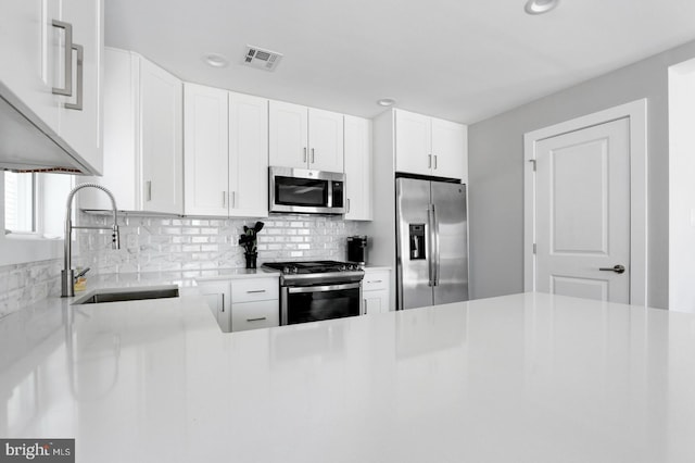 kitchen featuring white cabinets, appliances with stainless steel finishes, decorative backsplash, and sink