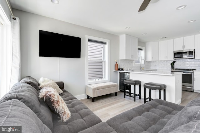 living room with ceiling fan, light hardwood / wood-style floors, sink, and wine cooler