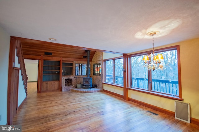 unfurnished living room featuring hardwood / wood-style floors, a wood stove, radiator heating unit, and an inviting chandelier