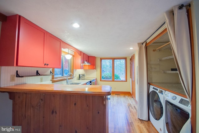 kitchen featuring stainless steel electric stove, sink, washer and dryer, light hardwood / wood-style floors, and kitchen peninsula