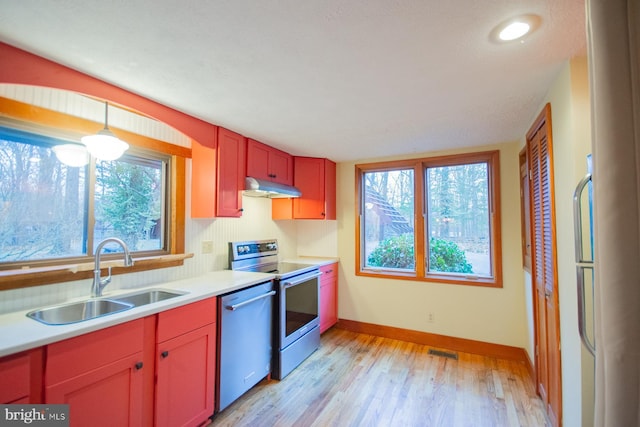 kitchen featuring hanging light fixtures, sink, stainless steel appliances, and light hardwood / wood-style flooring