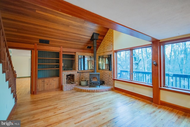 unfurnished living room with a wood stove, vaulted ceiling, and light wood-type flooring