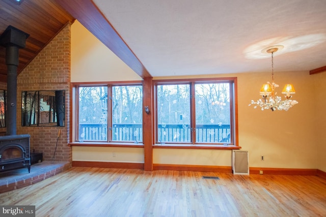 unfurnished living room with a healthy amount of sunlight, wood-type flooring, a wood stove, and a chandelier