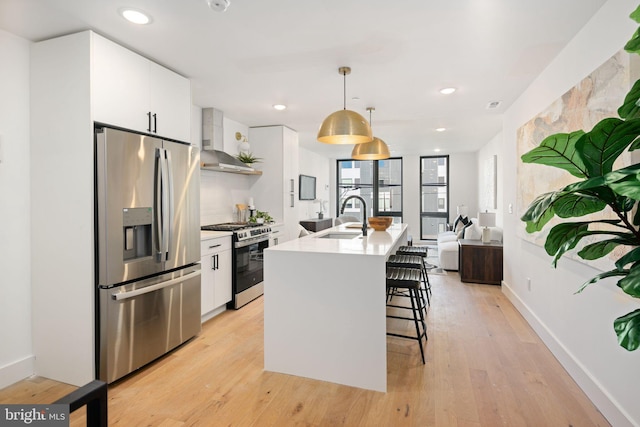 kitchen featuring pendant lighting, stainless steel appliances, white cabinetry, and wall chimney range hood