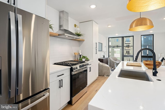 kitchen featuring white cabinetry, wall chimney range hood, light hardwood / wood-style flooring, decorative light fixtures, and appliances with stainless steel finishes