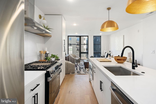 kitchen featuring white cabinets, hanging light fixtures, light hardwood / wood-style flooring, wall chimney exhaust hood, and appliances with stainless steel finishes