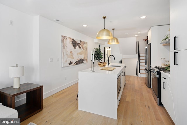 kitchen featuring decorative light fixtures, white cabinetry, an island with sink, and appliances with stainless steel finishes