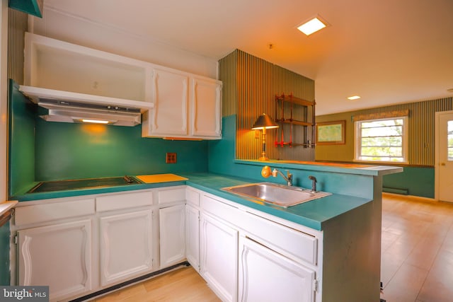 kitchen with kitchen peninsula, ventilation hood, sink, stovetop, and white cabinetry