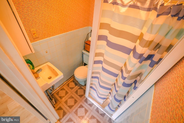 bathroom featuring a shower with curtain, toilet, tile walls, and sink