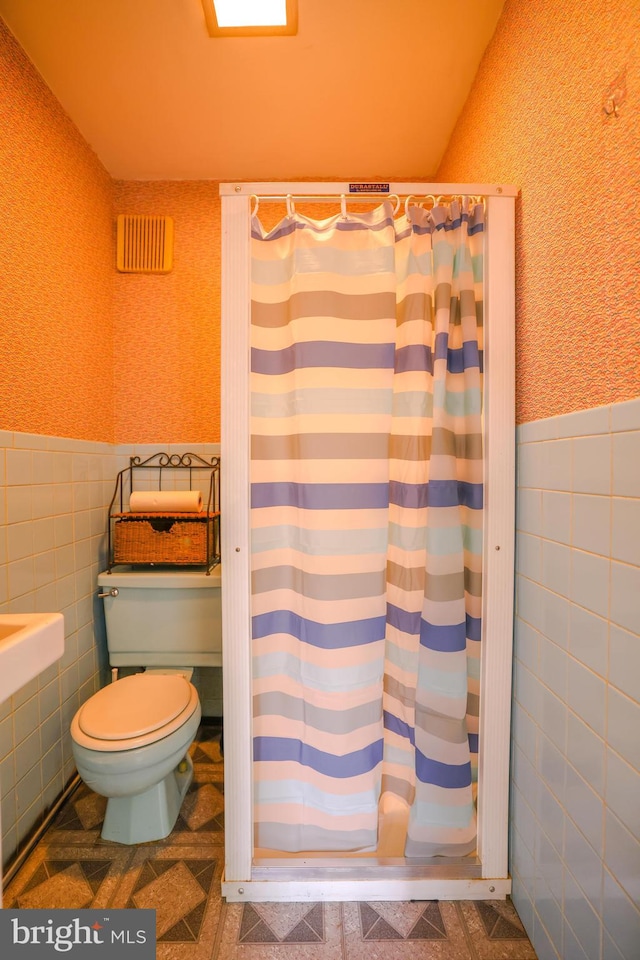 bathroom with toilet and tile walls